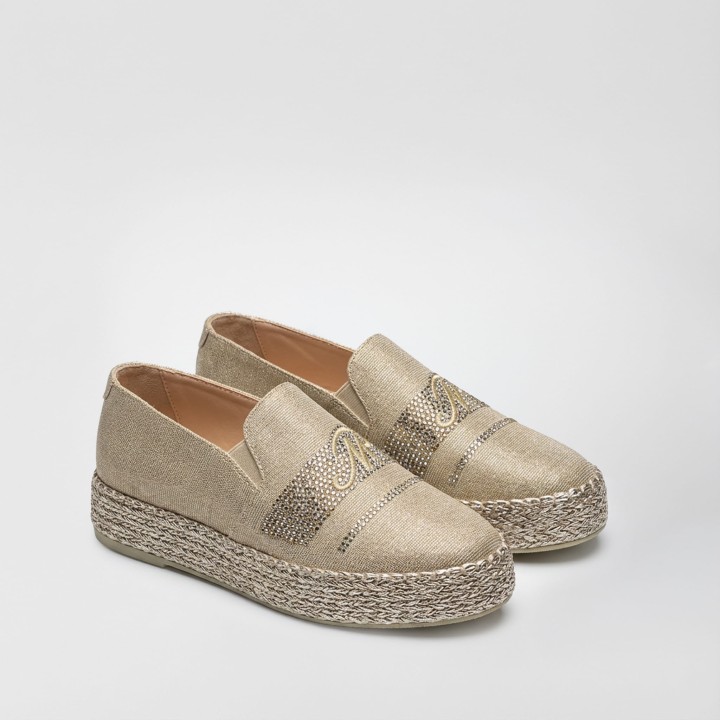 Złote espadryle na wysokiej plecionej platformie, ujęcie z boku. Cholewka z połyskującego materiału zdobiona pasami kryształków oraz haftowanym logo MP. Eleganckie buty typu slip-on na białym tle.